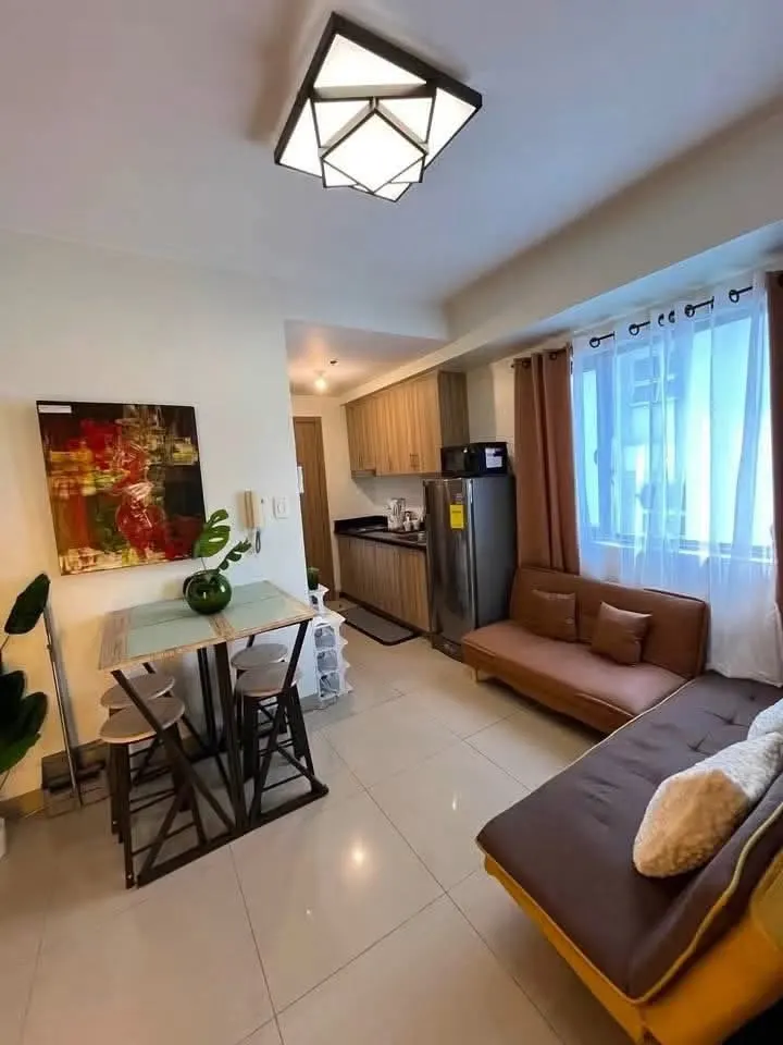 Living area with a sofa bed, a dining table by the window and the kitchen beyond