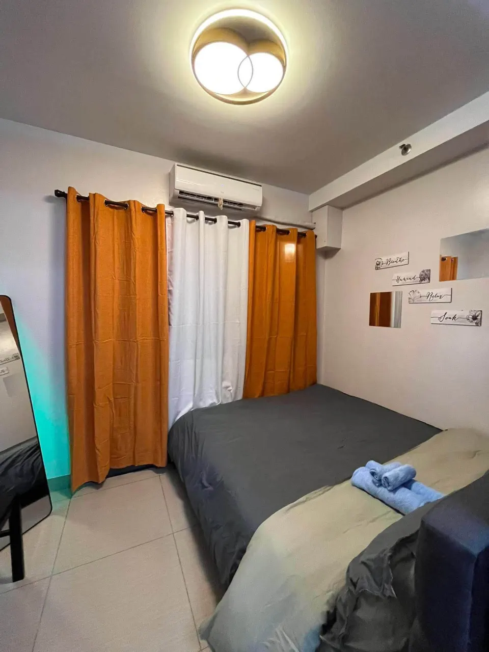 Bed by the window with orange curtains and air conditioning